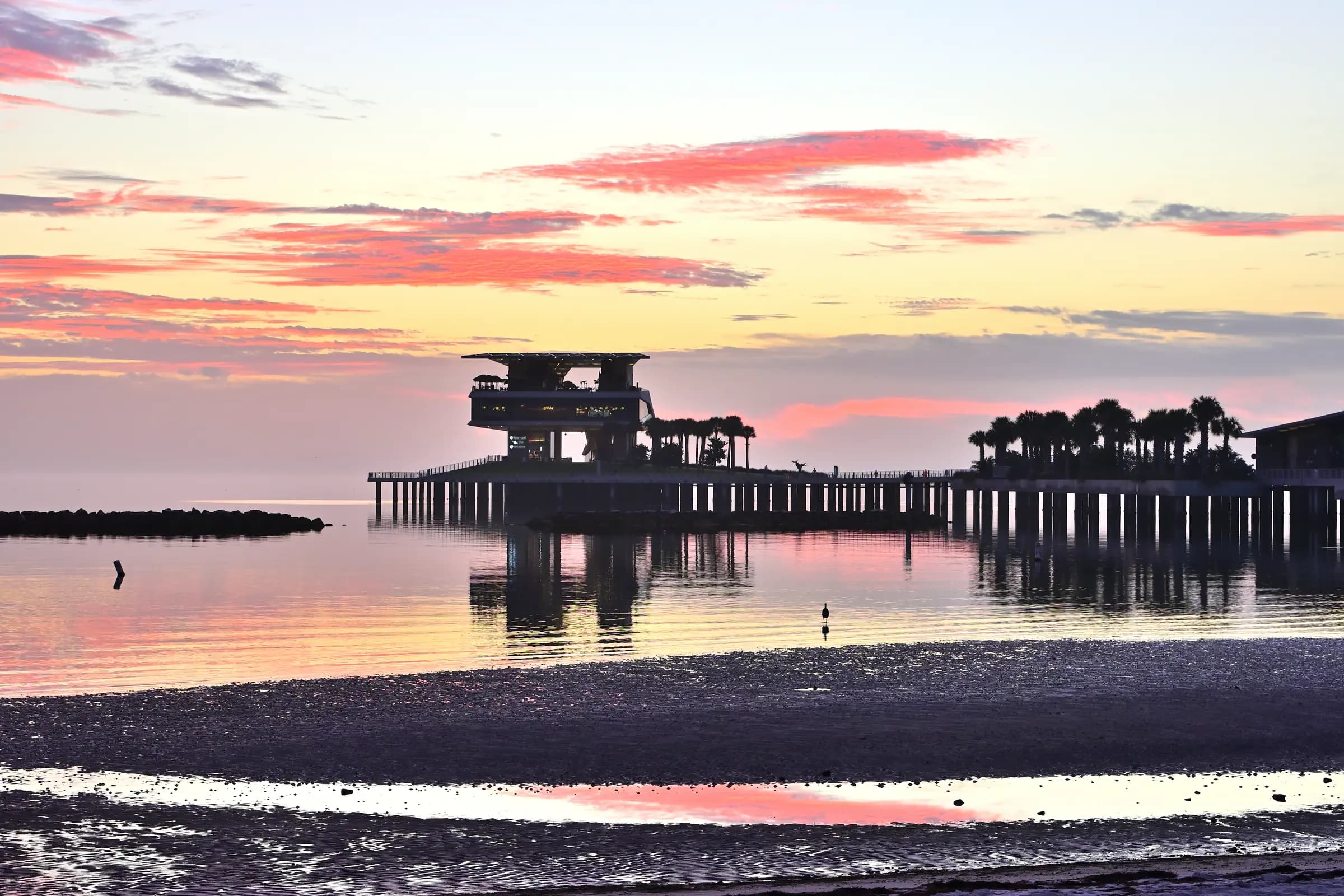 The St. Pete Pier silhouetted against a pink and gold sunrise over calm Tampa Bay.